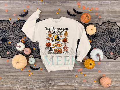 White sweatshirt with Halloween-themed design on a wooden surface with pumpkins and spider webs.